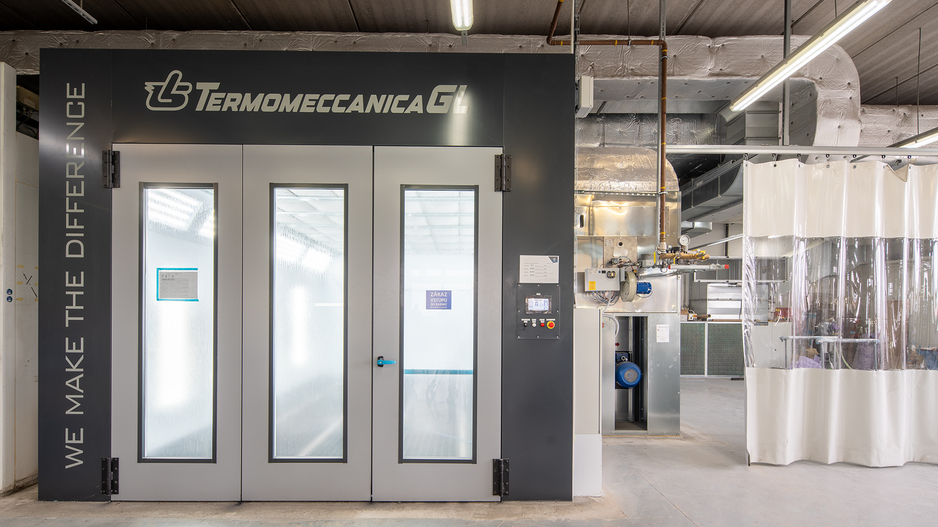 Čelní pohled na nový lakovací box Termomeccanica s rekuperační jednotkou pro významnou úsporu energie, vpravo přípravné stání oddělené od sousedních lakovacích technologií plentou.